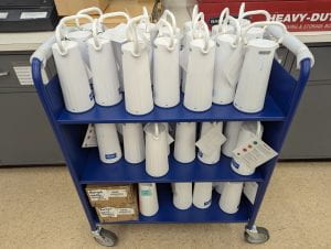 Many white cylinder-shaped battery units sitting on a cart in a staff workroom.